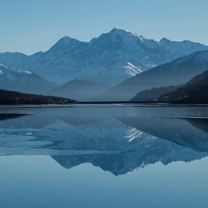 Snow-covered mountains reflecting on a calm lake beneath a clear blue sky, evoking stillness and tranquility.